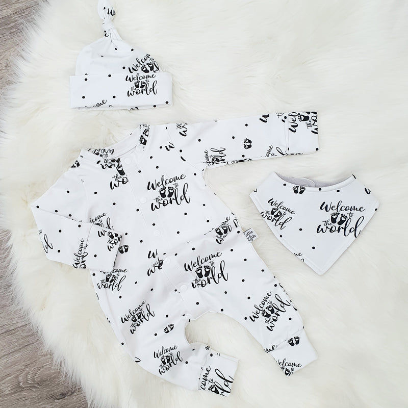 Monochrome newborn baby coming home outfit. White handmade romper with 'welcome to the wold' text print details. The outfit is pictured with a coordinating hat and bib. Handmade in the UK by Lottie & Lysh