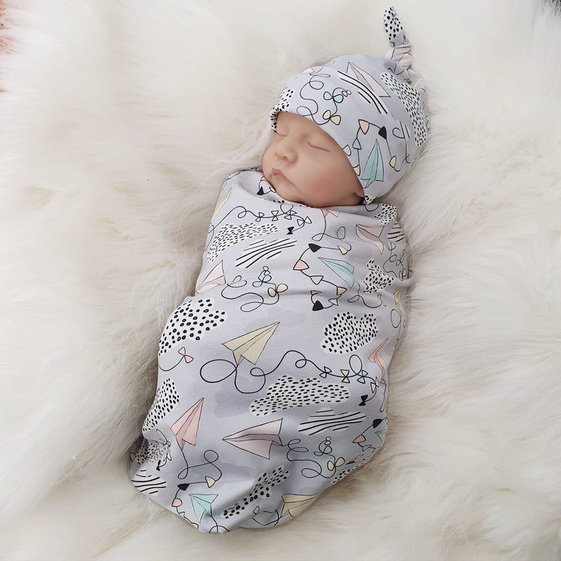 jersey baby swaddle set with paper planes print detail. Baby wearing matching knotted hat.